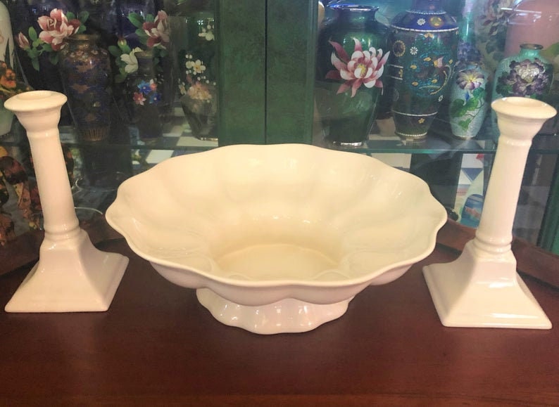 May include: Two white ceramic candle holders with square bases and a white ceramic bowl with a scalloped edge.