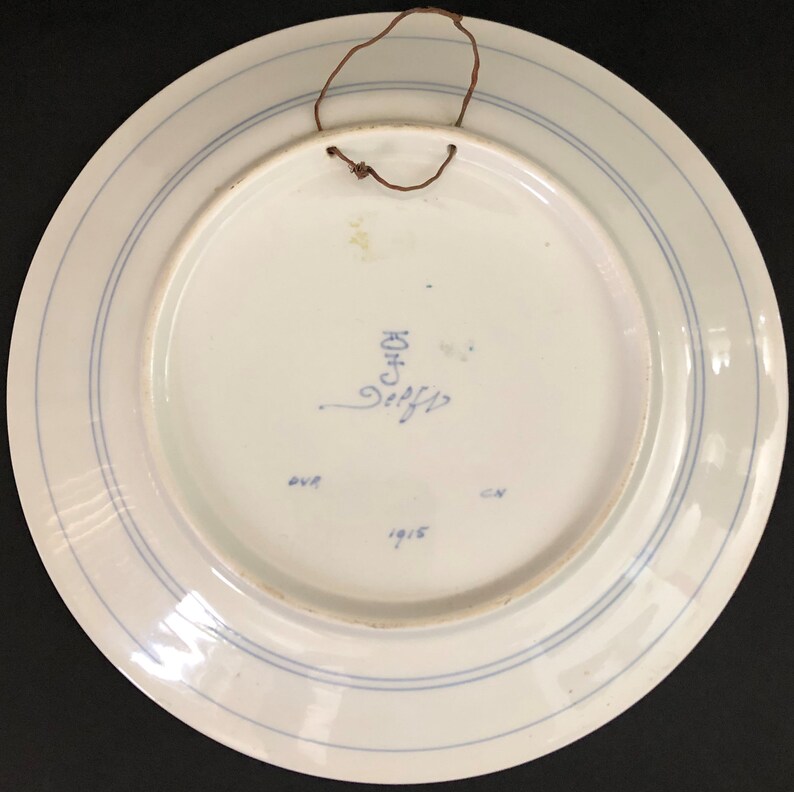 K&ouml;nnte beinhalten: Wei&szlig;e Keramikplatte mit blauem Rand und einer blauen Inschrift mit der Aufschrift "C.HOF" und "1915".