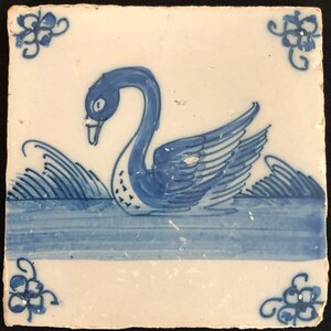 Puede incluir: Azulejo de cer&aacute;mica cuadrado y blanco con un dise&ntilde;o pintado a mano de un cisne azul nadando en agua azul. El azulejo tiene detalles florales azules decorativos en las esquinas. El cisne tiene un cuello largo y plumas de ala detalladas.