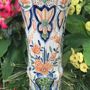 Puede incluir: Un jarr&oacute;n de cer&aacute;mica blanca con dise&ntilde;os florales azules, verdes y naranjas. El jarr&oacute;n tiene una parte superior acampanada y una base redonda. Est&aacute; decorado con un patr&oacute;n repetitivo de flores y hojas.