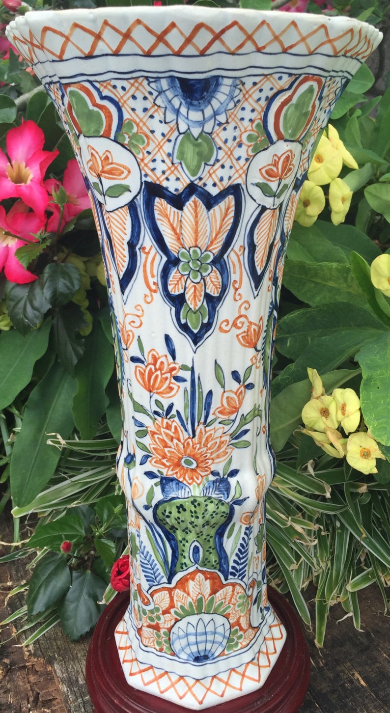 Puede incluir: Un jarr&oacute;n de cer&aacute;mica blanca con dise&ntilde;os florales azules, verdes y naranjas. El jarr&oacute;n tiene una parte superior acampanada y una base redonda. Est&aacute; decorado con un patr&oacute;n repetitivo de flores y hojas.