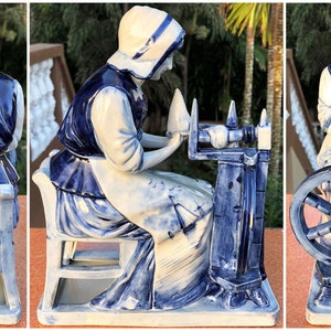 K&ouml;nnte beinhalten: Eine blau-wei&szlig;e Keramikfigur, die eine Frau an einem Spinnrad darstellt. Die Frau tr&auml;gt eine wei&szlig;e Haube, Bluse und Sch&uuml;rze mit einer dunkelblauen Weste. Das Spinnrad und der Stuhl sind ebenfalls blau und wei&szlig;. Ein dekorativer Artikel.