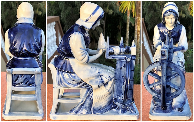 K&ouml;nnte beinhalten: Eine blau-wei&szlig;e Keramikfigur, die eine Frau an einem Spinnrad darstellt. Die Frau tr&auml;gt eine wei&szlig;e Haube, Bluse und Sch&uuml;rze mit einer dunkelblauen Weste. Das Spinnrad und der Stuhl sind ebenfalls blau und wei&szlig;. Ein dekorativer Artikel.