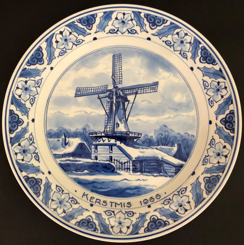 May include: Blue and white Delftware plate featuring a winter scene of a windmill and houses. The plate has a blue and white floral border and the text "KERSTMIS 1966".