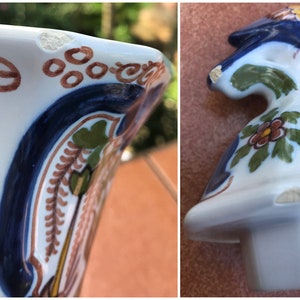 Puede incluir: Una jarra de cer&aacute;mica blanca con dise&ntilde;os florales pintados en azul, verde y marr&oacute;n. La jarra tiene un borde astillado y una peque&ntilde;a astilla en la base.