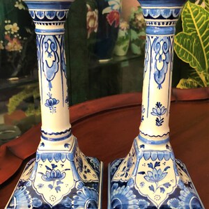 May include: Pair of blue and white ceramic candle holders with intricate floral designs. The holders have a square base and a tall, cylindrical body.