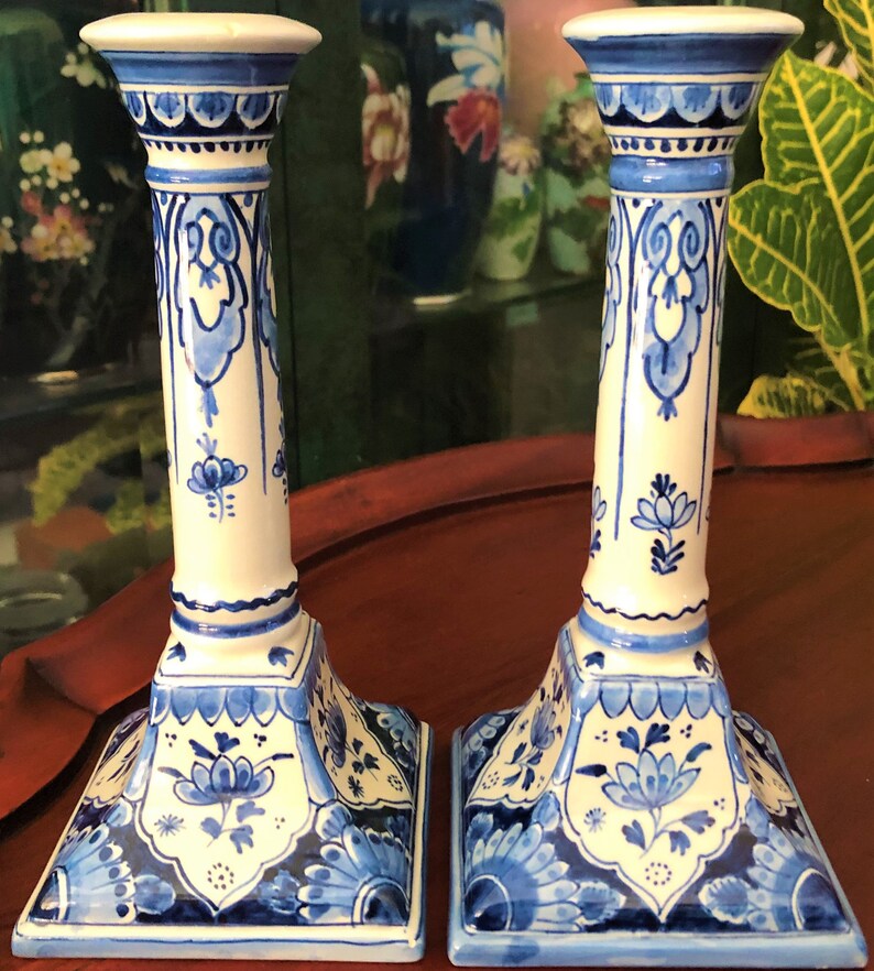May include: Pair of blue and white ceramic candle holders with intricate floral designs. The holders have a square base and a tall, cylindrical body.