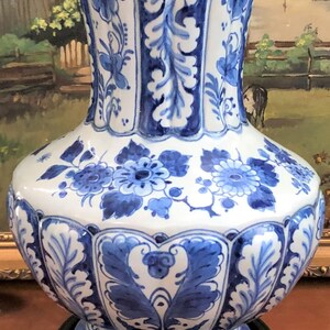 May include: A blue and white Delftware vase with a floral design. The vase has a wide base and a narrow neck. It is decorated with blue and white flowers and leaves.