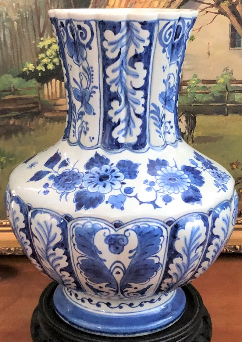 May include: A blue and white Delftware vase with a floral design. The vase has a wide base and a narrow neck. It is decorated with blue and white flowers and leaves.