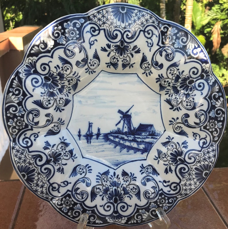 K&ouml;nnte beinhalten: Ein wei&szlig;er Teller aus Keramik mit einem blauen und wei&szlig;en Blumendesign. Die Mitte des Tellers zeigt eine blaue und wei&szlig;e Illustration einer Windm&uuml;hle und eines Kanals.