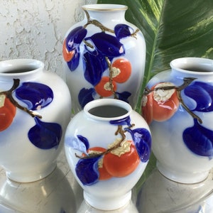 May include: Four white porcelain vases with blue and gold accents. Each vase features a hand-painted design of red persimmons on a branch with blue leaves.