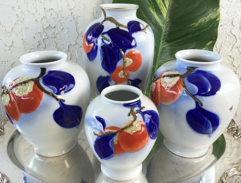 May include: Four white porcelain vases with blue and gold accents. Each vase features a hand-painted design of red persimmons on a branch with blue leaves.