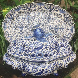 May include: A blue and white ceramic serving dish and matching lid with a floral and bird design. The dish has a scalloped edge and is decorated with intricate patterns. The lid features a bird-shaped handle.