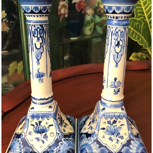 May include: A pair of blue and white ceramic candlestick holders with intricate floral designs. The candlesticks have a square base and a tall, cylindrical column.