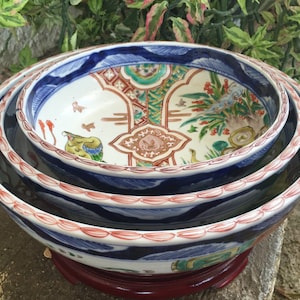 May include: A set of four nested, hand-painted ceramic bowls. The bowls feature intricate designs with blue, red, green, and brown colors. The rims have a red and white pattern, and the interiors showcase detailed scenes of birds and flowers.