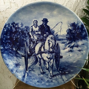 Pu&ograve; includere: Un piatto in ceramica blu e bianco con una scena di una coppia che viaggia in una carrozza trainata da un cavallo. Il piatto &egrave; decorato con un motivo floreale blu e bianco e il testo "naar een ontwerp" nell'angolo in basso a destra.