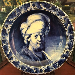 K&ouml;nnte beinhalten: Ein blauer und wei&szlig;er Teller aus Delft mit einem Portr&auml;t eines Mannes mit Turban. Der Teller hat einen dekorativen Rand aus Blumen und Bl&auml;ttern.