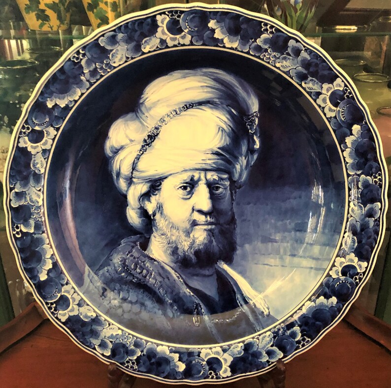 K&ouml;nnte beinhalten: Ein blauer und wei&szlig;er Teller aus Delft mit einem Portr&auml;t eines Mannes mit Turban. Der Teller hat einen dekorativen Rand aus Blumen und Bl&auml;ttern.