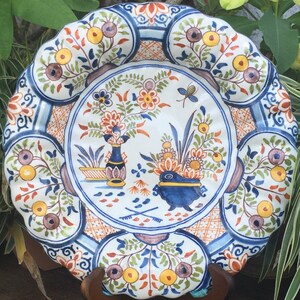 Puede incluir: Un plato de cer&aacute;mica blanco con un dise&ntilde;o floral azul y blanco. El plato tiene un borde festoneado y est&aacute; decorado con una variedad de flores, incluyendo rosas, tulipanes y lirios. El plato tambi&eacute;n est&aacute; decorado con un patr&oacute;n de cuadros azules y blancos.