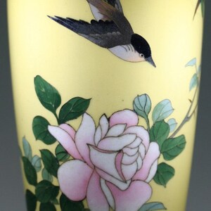 Pu&ograve; includere: Un vaso di ceramica giallo con un design di uccello e fiori. Il vaso ha un'ampia apertura e una base stretta. L'uccello &egrave; nero e grigio con il petto bianco. I fiori sono rosa e bianchi con foglie verdi.