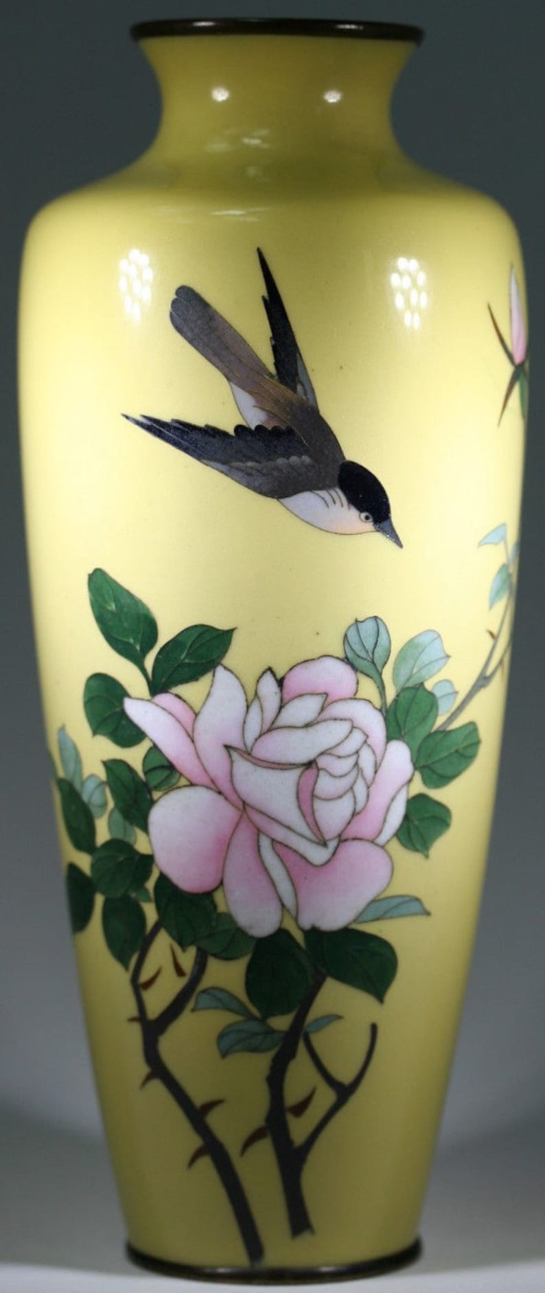 Pu&ograve; includere: Un vaso di ceramica giallo con un design di uccello e fiori. Il vaso ha un'ampia apertura e una base stretta. L'uccello &egrave; nero e grigio con il petto bianco. I fiori sono rosa e bianchi con foglie verdi.