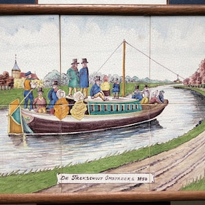 May include: A vintage tile painting depicting a canal scene with a boat full of people. The boat is being pulled by a rope attached to a horse on the towpath. The tile is titled "De Trekschuit Omstreeks 1850".