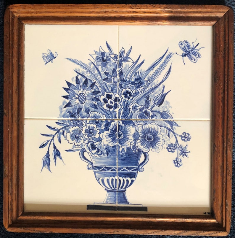 Puede incluir: Un azulejo de Delft azul y blanco que representa un jarr&oacute;n lleno de flores. El jarr&oacute;n tiene dos asas y est&aacute; decorado con un patr&oacute;n geom&eacute;trico. Las flores est&aacute;n dispuestas en un ramo e incluyen rosas, tulipanes y otras flores. Tambi&eacute;n se representan dos mariposas en el azulejo.