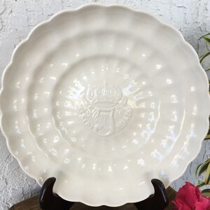 Puede incluir: Un plato de cer&aacute;mica blanco con un borde festoneado y un dise&ntilde;o en relieve en el centro. El dise&ntilde;o presenta una corona, un s&iacute;mbolo y la palabra "OSPEDALE".