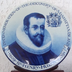 May include: A blue and white ceramic plate commemorating the discovery of Manhattan Island by Henry Hudson. The plate features a portrait of a man with a beard and a ruffled collar, with text that reads "In Commemoration of the Discovery of Manhattan Island 1609 by Henry Hudson 1909."