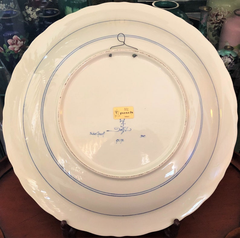Puede incluir: Un plato de cer&aacute;mica blanco con detalles azules y dorados. La parte posterior del plato tiene una etiqueta que dice "W. Pasch Gold" y "Nide-Graef 91/7 3C".