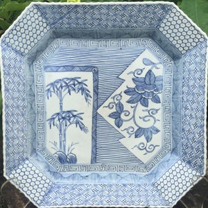 May include: Square ceramic serving dish with a blue and white floral and bamboo design. The dish has an octagonal shape with geometric patterns on the border. The interior features a bamboo and floral motif.