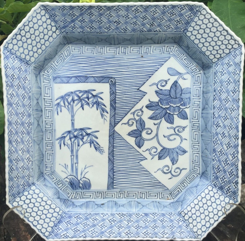 May include: Square ceramic serving dish with a blue and white floral and bamboo design. The dish has an octagonal shape with geometric patterns on the border. The interior features a bamboo and floral motif.