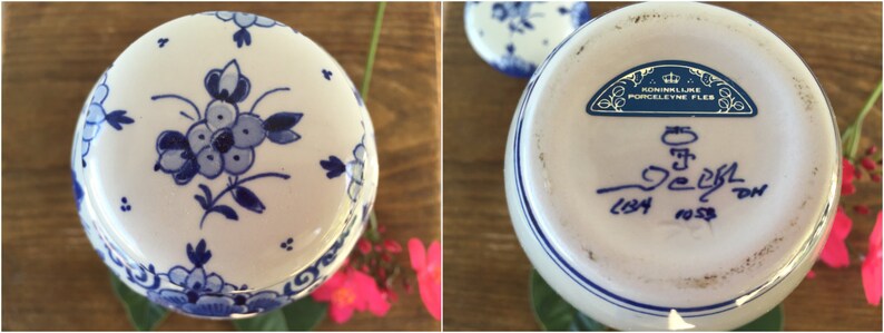 May include: A white ceramic vase with blue floral designs and a blue rim. The bottom of the vase has a blue stamp that reads "KONINKLIJKE PORCELEYNE FLES" and other text. The vase is on a wooden surface.