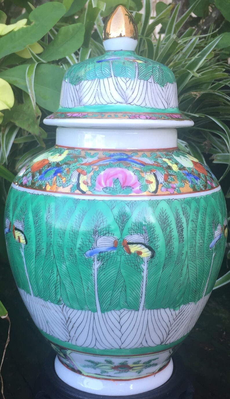 Op de afbeelding: Een witte porseleinen Chinese gemberpot met een groen en gouden bloemenmotief. De deksel heeft een gouden knop en een groen en wit bloemenmotief.