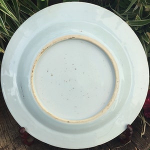 Op de afbeelding: De onderkant van een wit porseleinen bord met een licht verhoogde rand. Het bord heeft een glad, geglazuurd oppervlak met een paar kleine bruine vlekken.