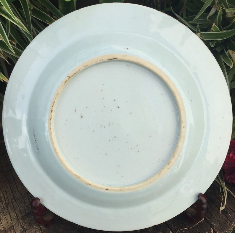 Op de afbeelding: De onderkant van een wit porseleinen bord met een licht verhoogde rand. Het bord heeft een glad, geglazuurd oppervlak met een paar kleine bruine vlekken.