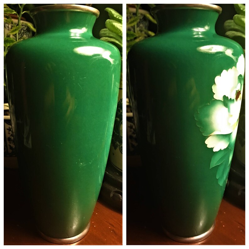 Puede incluir: Dos jarrones de cer&aacute;mica verde con bordes plateados. Un jarr&oacute;n tiene un dise&ntilde;o floral blanco con hojas verdes. Ambos jarrones est&aacute;n sobre una superficie de madera.