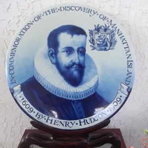 May include: A blue and white ceramic plate commemorating the discovery of Manhattan Island by Henry Hudson in 1609. The plate features a portrait of Henry Hudson and a coat of arms with a ship.