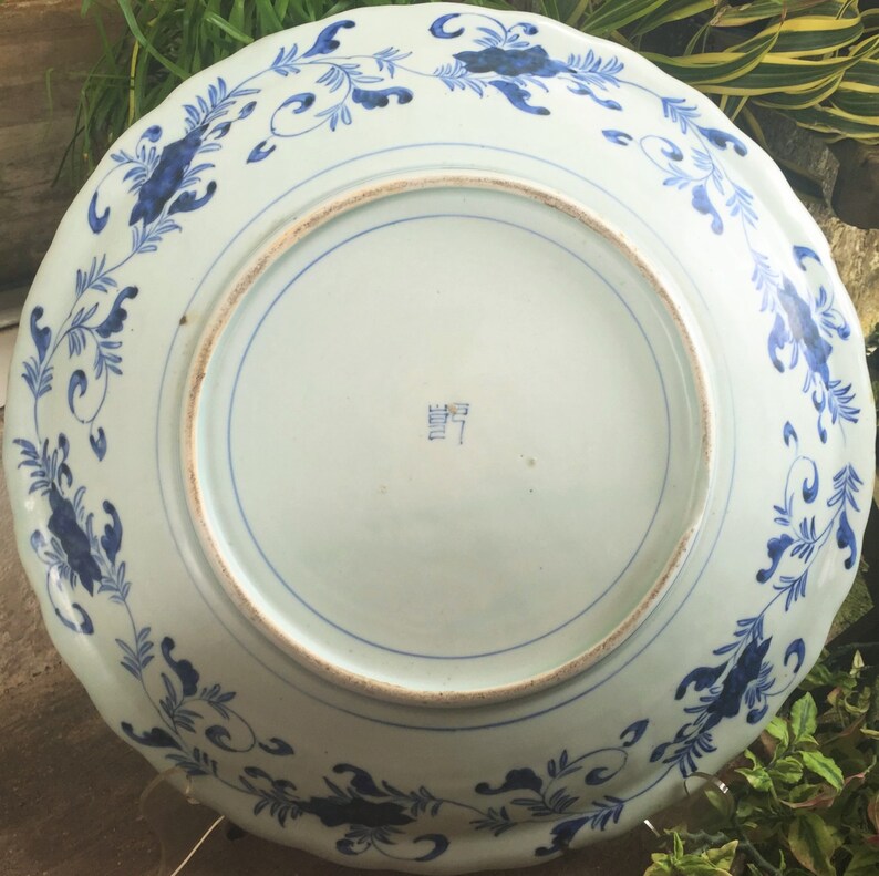 Op de afbeelding: Een wit keramiek bord met een blauw en wit bloemenpatroon. Het bord heeft een gegolfde rand en een markering aan de onderkant die "MADE IN JAPAN" luidt.