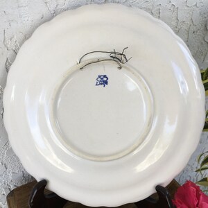 Puede incluir: Plato de cer&aacute;mica blanco con un dise&ntilde;o floral azul y blanco. La parte posterior del plato tiene un sello azul que dice "Delft" con una "B" estilizada encima.