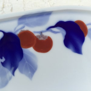 May include: A white ceramic plate with a blue and red floral design. The design features blue leaves and red fruit.