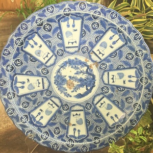 Op de afbeelding: Een grote, ronde, blauw-witte keramische plaat met een decoratief ontwerp. De plaat heeft een centraal bloemenmotief omringd door acht herhalende geometrische patronen.