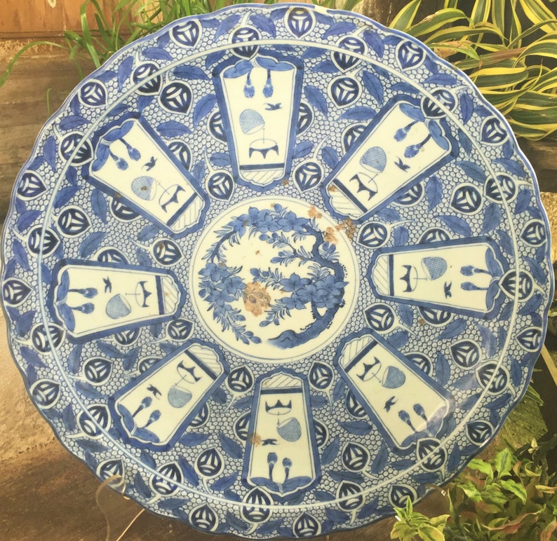 Op de afbeelding: Een grote, ronde, blauw-witte keramische plaat met een decoratief ontwerp. De plaat heeft een centraal bloemenmotief omringd door acht herhalende geometrische patronen.