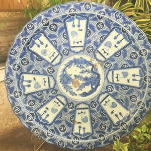 Op de afbeelding: Een grote, ronde, blauw-witte keramische plaat met een decoratief ontwerp. De plaat heeft een gegolfde rand en heeft een centraal bloemenmotief omringd door herhalende geometrische patronen.