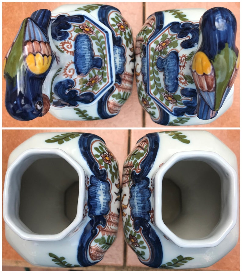 Puede incluir: Par de jarrones vintage de Delftware con dise&ntilde;o de p&aacute;jaro. Los jarrones son blancos con patrones florales azules, verdes y marrones. Los p&aacute;jaros son azules con detalles amarillos y marrones.