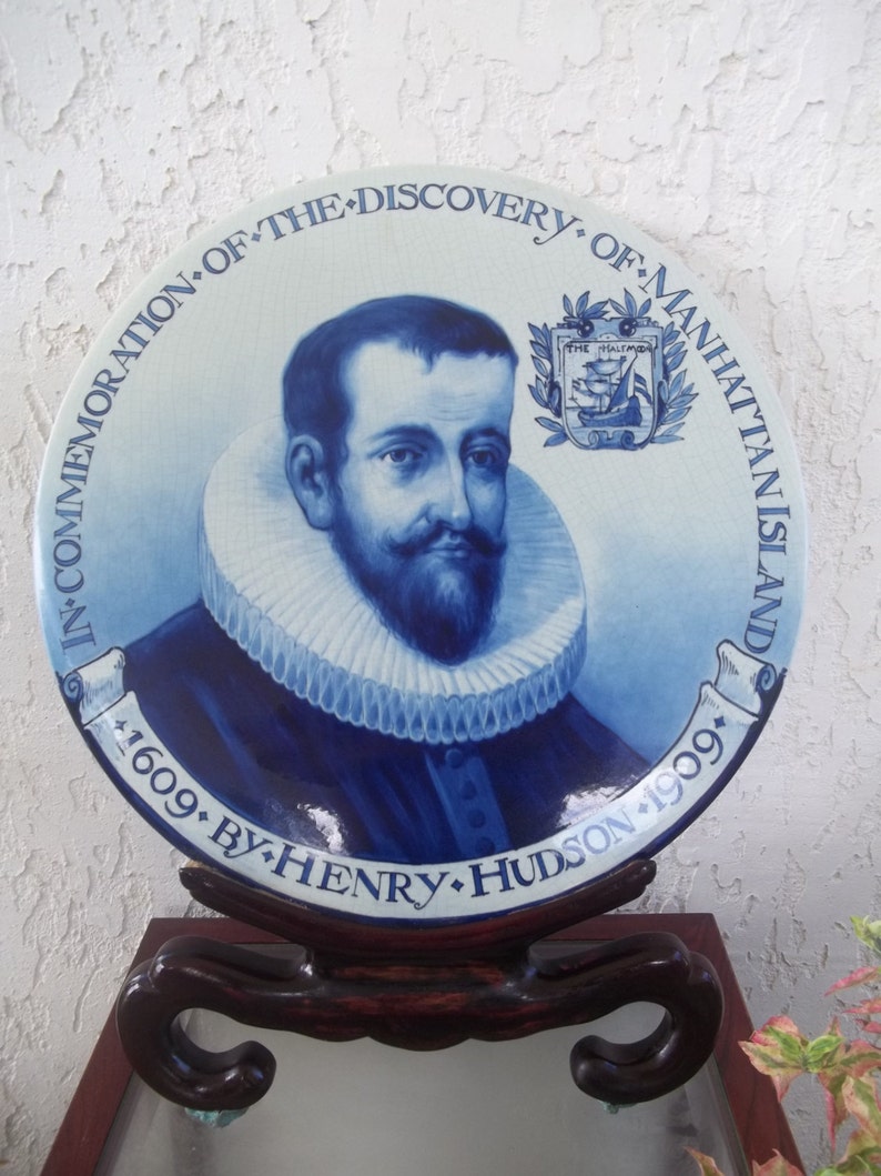 May include: A blue and white ceramic plate commemorating the discovery of Manhattan Island by Henry Hudson in 1609. The plate features a portrait of Henry Hudson and a coat of arms with a ship.