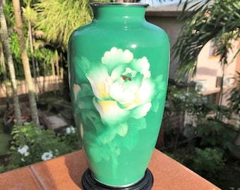 May include: A green ceramic vase with a white flower design. The vase has a glossy finish and a round shape.