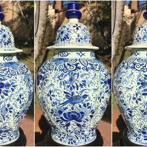 May include: A set of three matching blue and white ceramic ginger jars with lids. The jars feature intricate floral and bird patterns in a classic Delftware style. The jars are displayed on a dark surface.