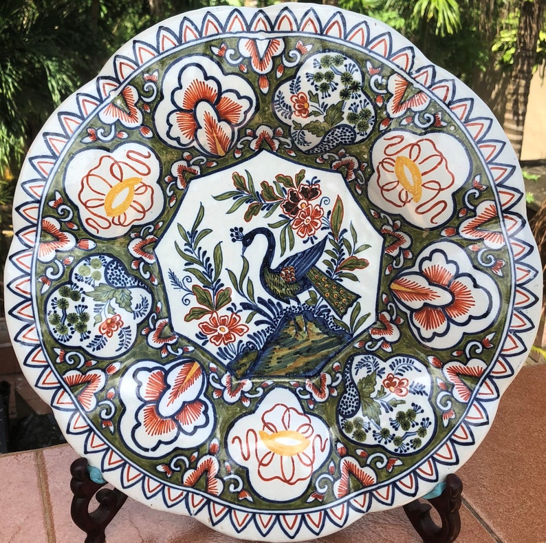 K&ouml;nnte beinhalten: Ein wei&szlig;er Teller aus Keramik mit gewelltem Rand zeigt ein farbenfrohes Blumen- und Pfauenmotiv. Der Teller ist mit blauer, gr&uuml;ner, roter und gelber Farbe verziert.