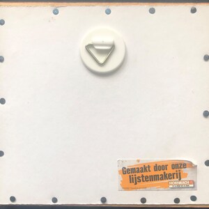 Puede incluir: Parte trasera de un cuadro enmarcado con un fondo blanco, un colgador de metal y una etiqueta con texto en holand&eacute;s. El marco es negro con borde de madera y peque&ntilde;as tachuelas negras.